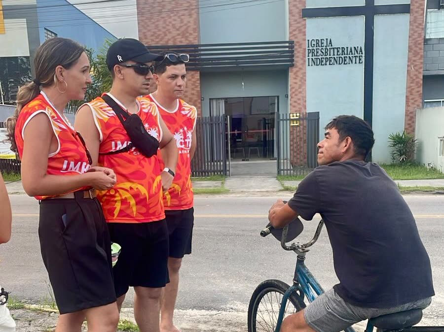 Três voluntários conversando com um rapaz de bicicleta na rua