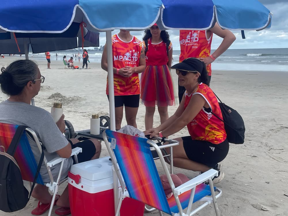 Voluntárias conversando com uma família sob o guarda-sol na praia